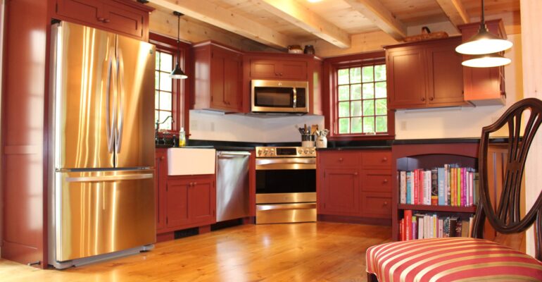 View of country kitchen with timbered ceiling and wide board floors.